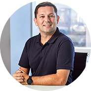 Homem sorridente em ambiente de escritório, vestindo camisa preta, transmitindo segurança e conforto em seu espaço de trabalho.